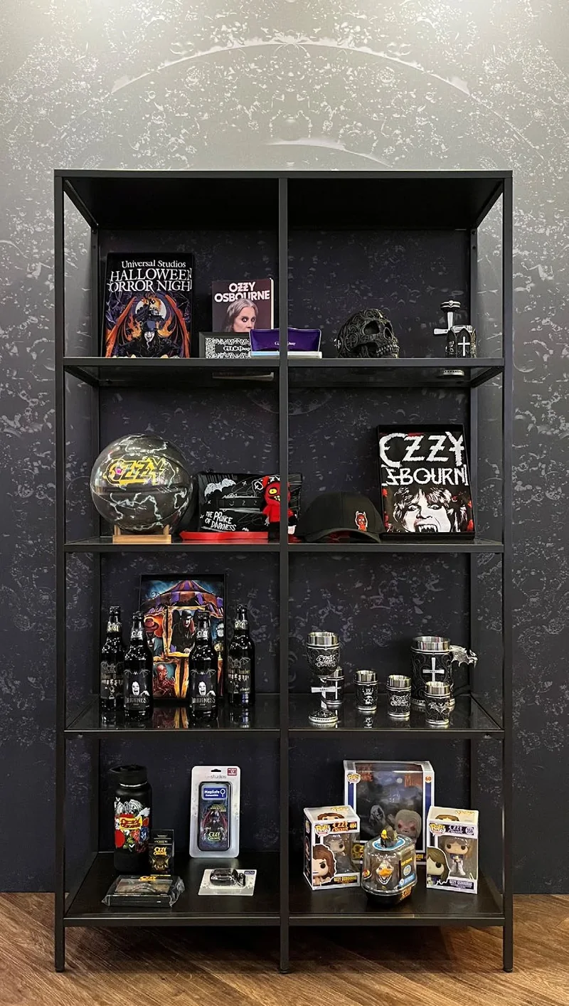 Ozzy Osbourne exhibition display with books, apparel, drinkware and collectible figures on black shelving.